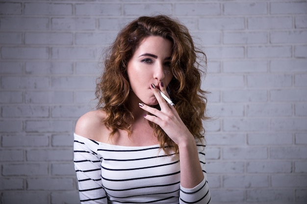 Belle jeune femme cigarette sur mur de briques blanches