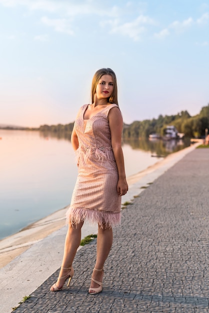 Belle jeune femme contre le coucher du soleil sur le lac