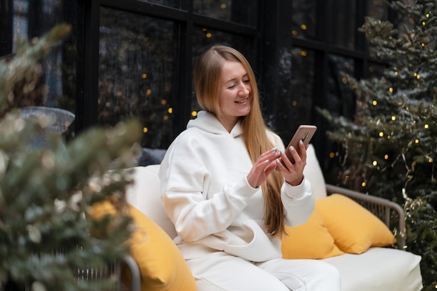 Belle jeune femme en costume d'hiver se promène parmi les sapins et parle au téléphone