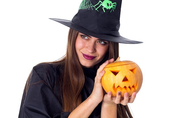 Belle jeune femme en costume noir de sorcière avec chapeau noir tenant une citrouille