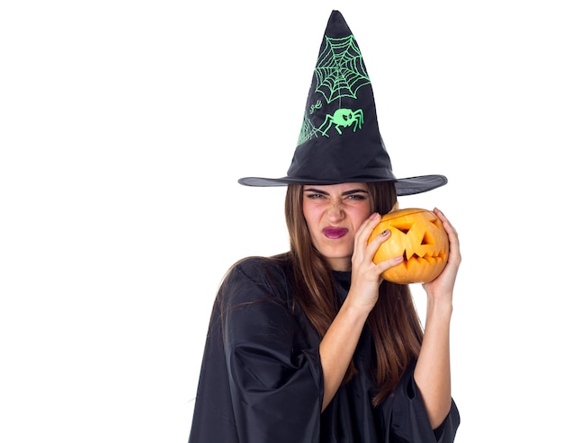 Belle jeune femme en costume noir de sorcière avec chapeau noir tenant une citrouille