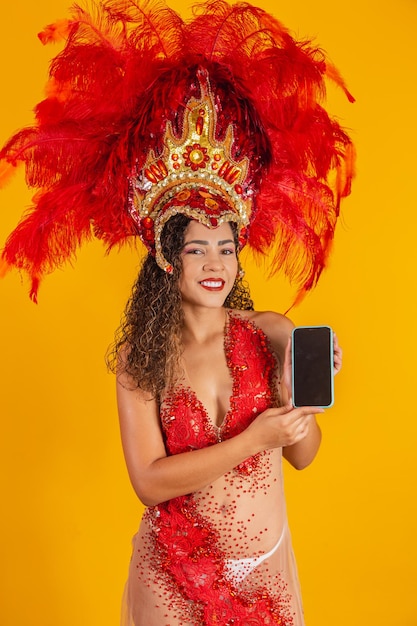 Belle jeune femme en costume de plume de carnaval spécial tenant un smartphone avec écran blanc avec un espace pour le texte. Carnaval virtuel, promotion et publicités. Verticale