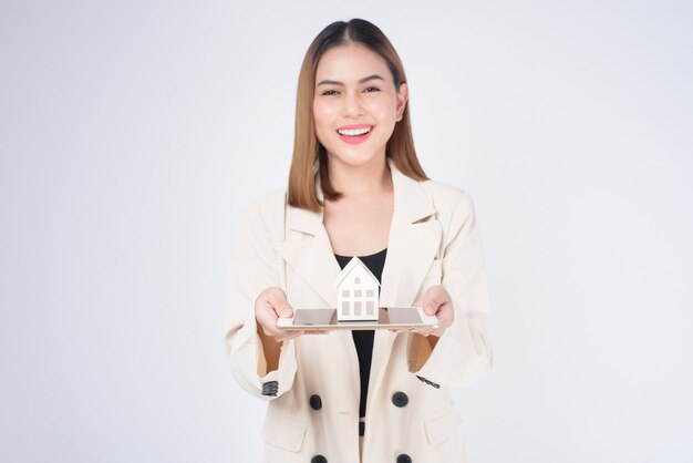 Belle jeune femme en costume tenant une petite maison modèle sur fond blanc studio