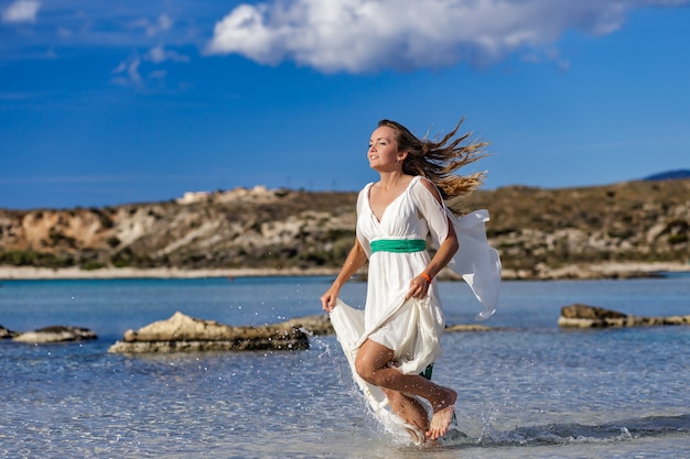 Une belle jeune femme court la liberté à travers l'eau de mer