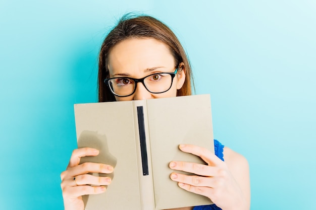 Belle jeune femme couvrant son visage avec un livre avec le concept de lecture de fond bleu