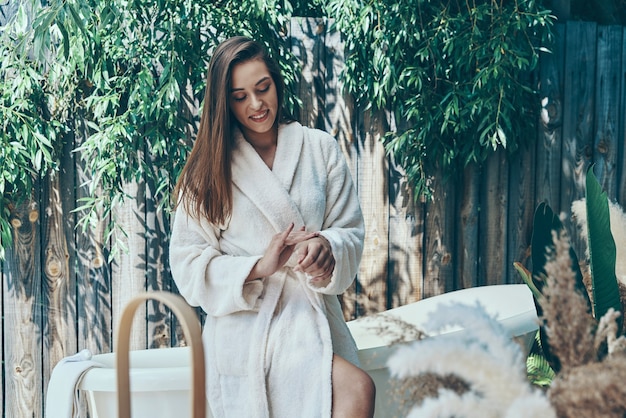 Belle jeune femme crème hydratante pour les mains tout en se penchant sur la baignoire à l'extérieur