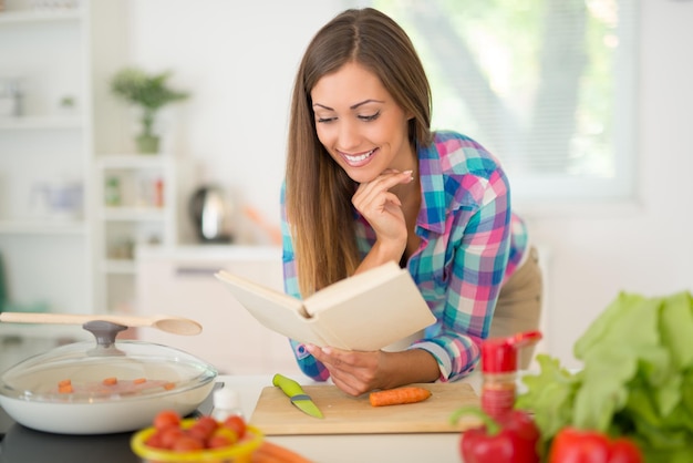 Belle jeune femme cuisinant un repas sain dans la cuisine domestique. Elle lit la recette dans le livre de cuisine.