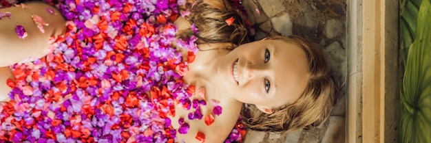 Belle jeune femme dans un bain avec des pétales de fleurs tropicales et des traitements de spa aux huiles aromatiques pour