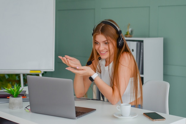 belle jeune femme dans un casque communique en ligne avec un ordinateur portable dans le bureau lifestyle f