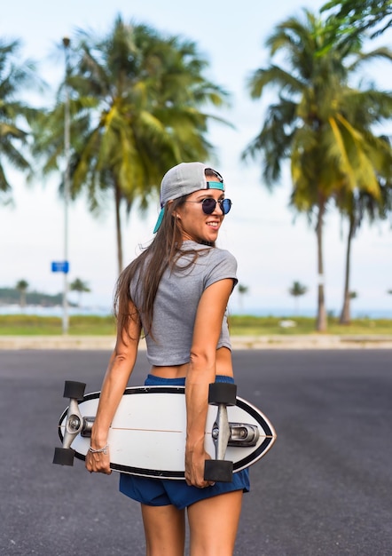 Une belle jeune femme dans un chapeau debout et tenant un skateboard avec un visage frais