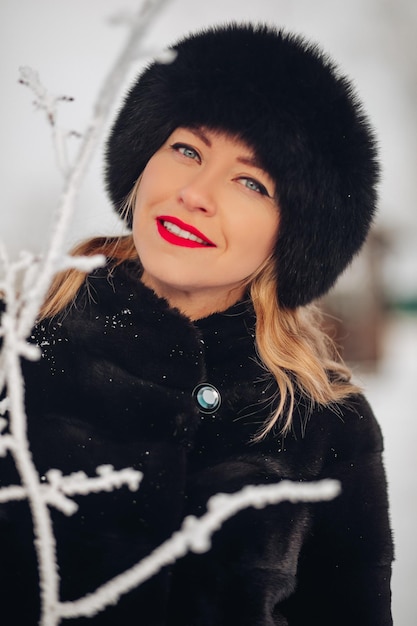 Une belle jeune femme dans un chapeau de fourrure noire et un portrait de manteau de fourrure Une jolie fille russe sourit et regarde dans le cadre des lèvres rouges maquillage lumineux