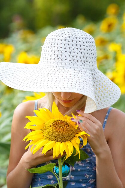 Belle jeune femme dans un chapeau et des lunettes sur un champ de tournesols.