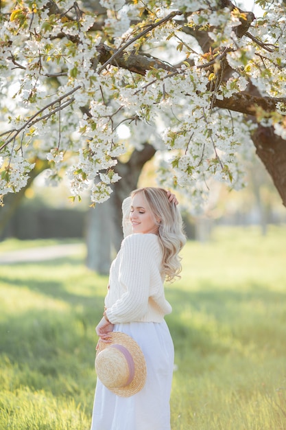 La belle jeune femme dans un chapeau en osier se repose sur un pique-nique dans un jardin fleuri