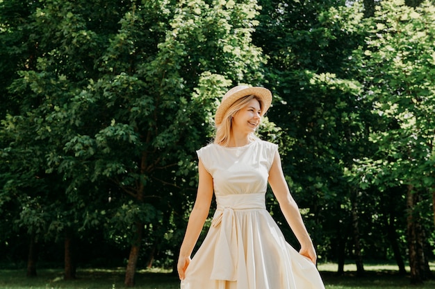 Belle jeune femme dans un chapeau de paille et une robe blanche dans un parc verdoyant ou une forêt un jour d'été