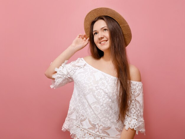 belle jeune femme dans un chapeau de paille sur la tête sourit sur un mur rose