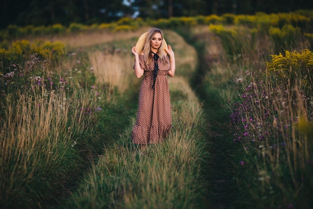 Belle jeune femme dans un chapeau et une robe se promène dans la nature en automne.