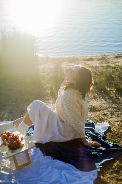 Photo belle jeune femme dans un chaud cardigan tricoté sur un confortable pique-nique d'automne au bord du lac avec des pâtisseries aux fruits