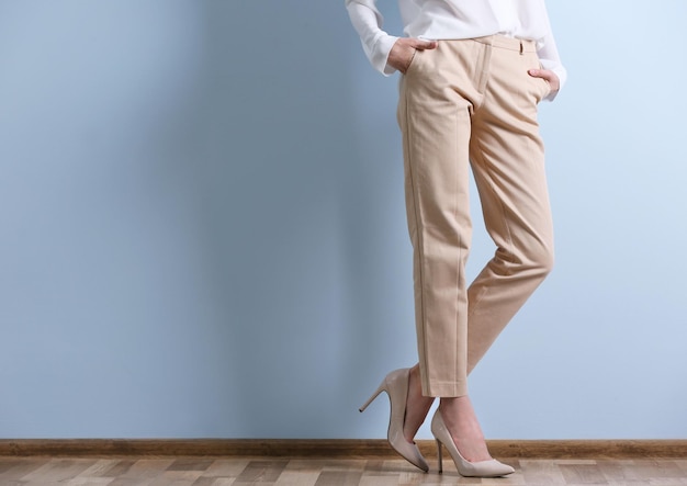 Belle jeune femme dans une chemise blanche et un pantalon beige sur fond de mur bleu