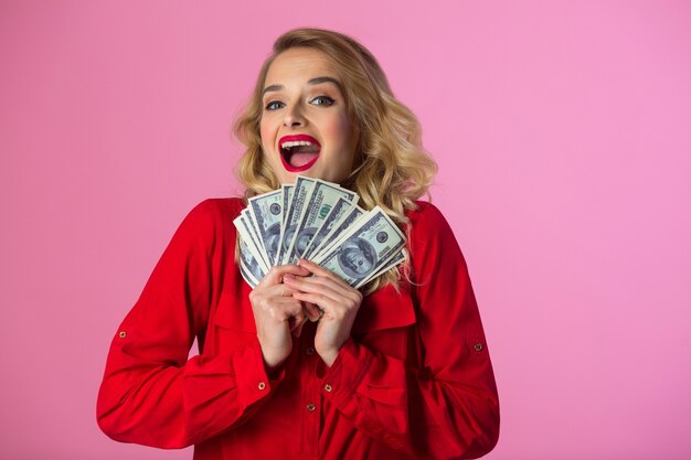 Belle jeune femme dans une chemise rouge avec des dollars dans leurs mains sur un mur rose