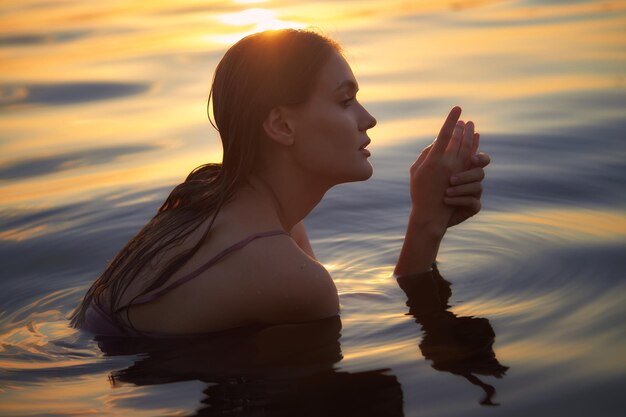 Belle jeune femme dans l'eau du lac en robe d'été au coucher du soleil