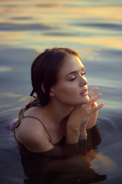 Belle jeune femme dans l'eau du lac en robe d'été au coucher du soleil