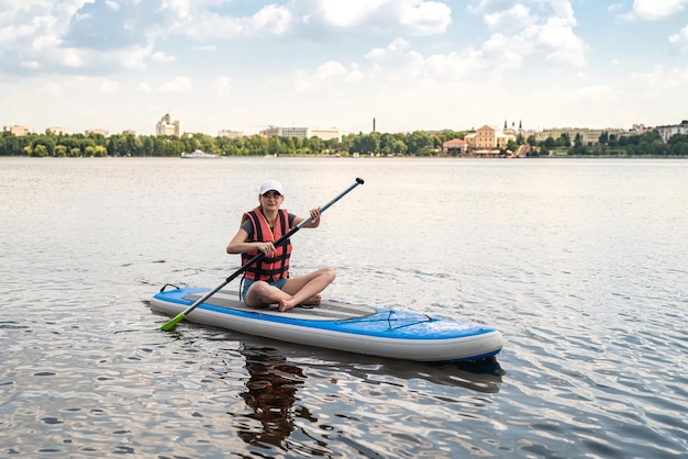 Belle jeune femme dans un gilet de protection apprend à nager dans le grenier sur un lac de la ville Mode de vie actif Heure d'été Le concept de mener une vie saine