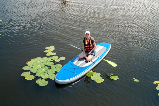 Belle jeune femme dans un gilet de protection apprend à nager sur une planche sup sur un lac de la ville