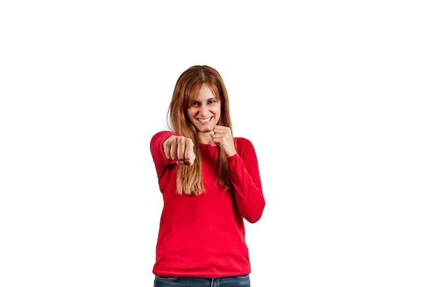 Belle jeune femme dans un pull rouge, frappant avec son poing, isolé sur un mur blanc.