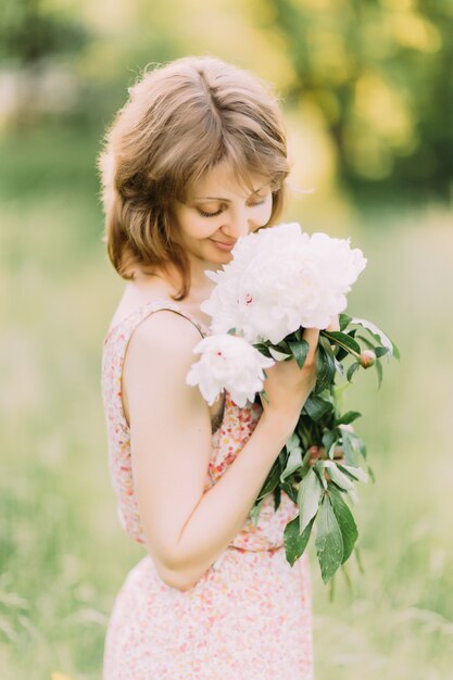 Belle jeune femme dans une robe d'été avec des pivoines