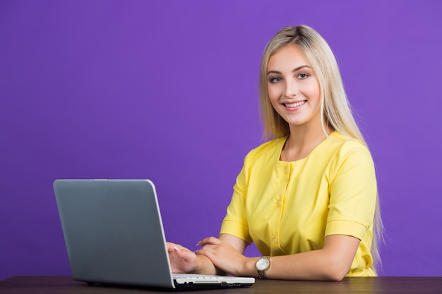 Belle jeune femme dans une robe jaune est assise à une table avec un ordinateur portable