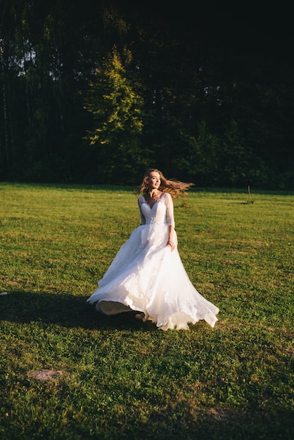 Belle jeune femme dans une robe de mariée blanche et des bottes noires au coucher du soleil.