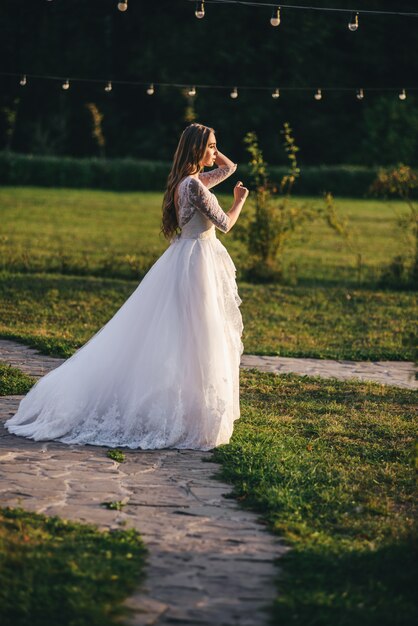 Belle jeune femme dans une robe de mariée blanche et des bottes noires au coucher du soleil.