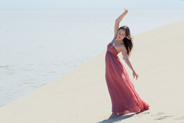 Une belle jeune femme dans une robe rose se promène sur les dunes de sable