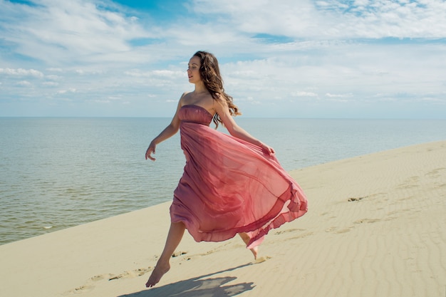 Une belle jeune femme dans une robe rose se promène sur les dunes de sable