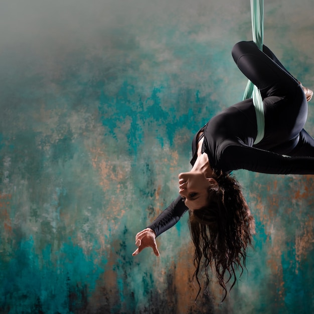 Une belle jeune femme dans un survêtement noir serré fait du yoga sur une suspension