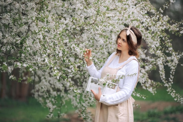 Une belle jeune femme dans le tablier profite de la vie dans un jardin fleuri au printemps avec des arbres en fleurs