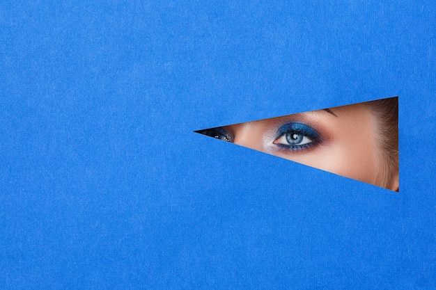 Photo belle jeune femme dans un trou de papier bleu, beau maquillage lumineux,