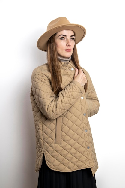 Belle jeune femme dans une veste avec un chapeau sur le fond d'un mur blanc