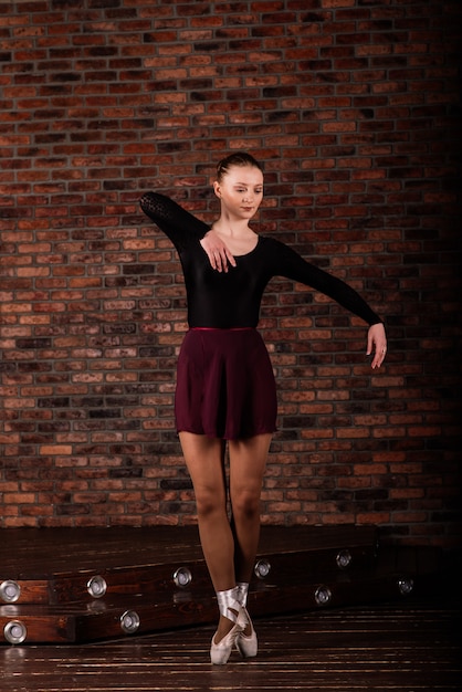 Belle jeune femme danseuse de ballet classique sur des pointes portant un justaucorps noir et une jupe sur un fond de brique