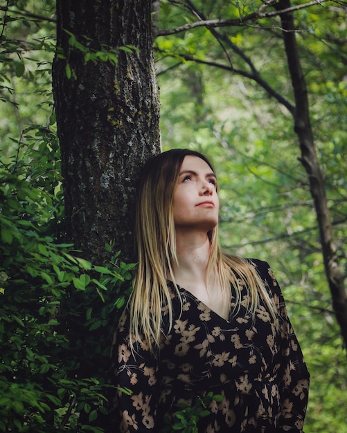 Photo une belle jeune femme debout contre un tronc d'arbre dans la forêt