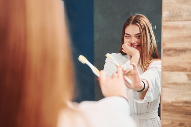 Belle jeune femme debout dans la salle de bain près du miroir et se brosser les dents