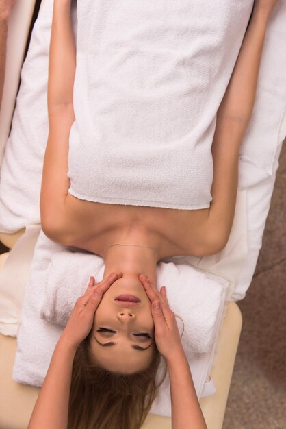 Belle jeune femme détendue recevant un massage de la tête dans un centre de spa