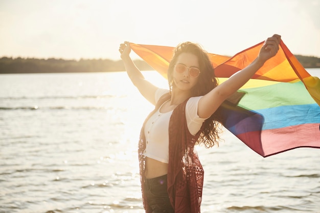 Belle jeune femme avec drapeau arc-en-ciel à la plage