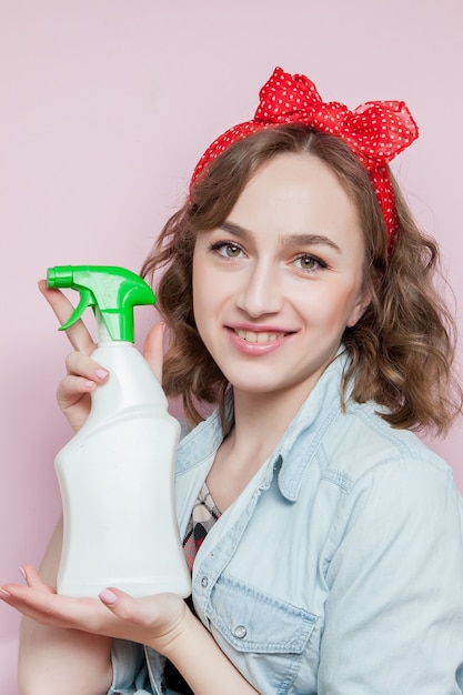 Belle jeune femme avec du maquillage et une coiffure avec des outils de nettoyage sur fond rose