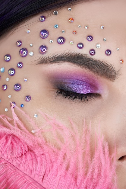 Belle jeune femme avec du maquillage pour les yeux rouges violets, gros plan de maquillage de beauté lumineuse, gros strass autour de l'œil. Sourcils épais et uniformes