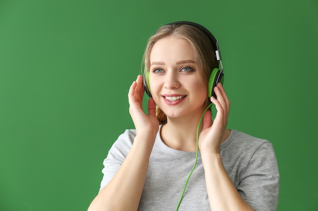 Belle jeune femme écoutant de la musique contre le mur vert