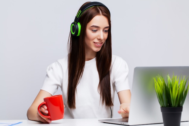 Belle jeune femme écoutant de la musique dans les écouteurs travaillant sur ordinateur portable au bureau