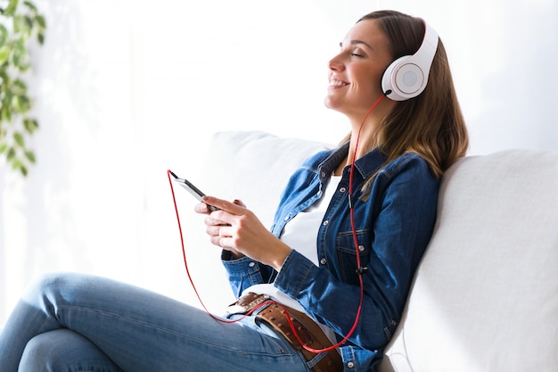 Belle jeune femme écoutant de la musique avec un téléphone portable à la maison.