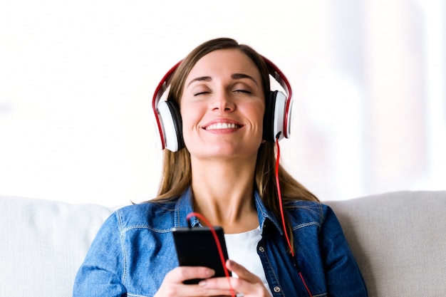 Belle jeune femme écoutant de la musique avec un téléphone portable à la maison.