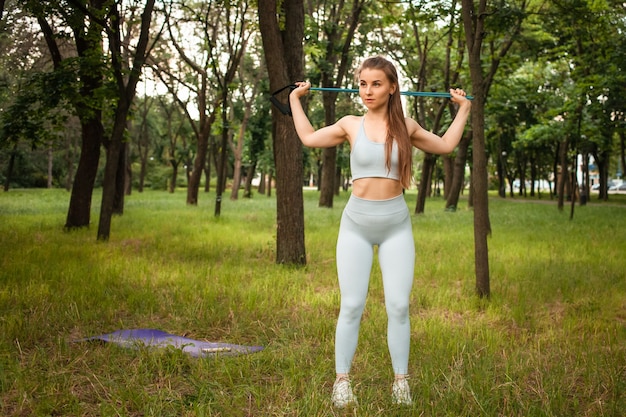 Une belle jeune femme effectue un exercice en plein air. Herbe, parc, entraînement sportif. Aptitude. Un extenseur. Équipement de sport, coucher de soleil. Un mode de vie sain, un corps musclé entraîné. Tapis de gymnastique